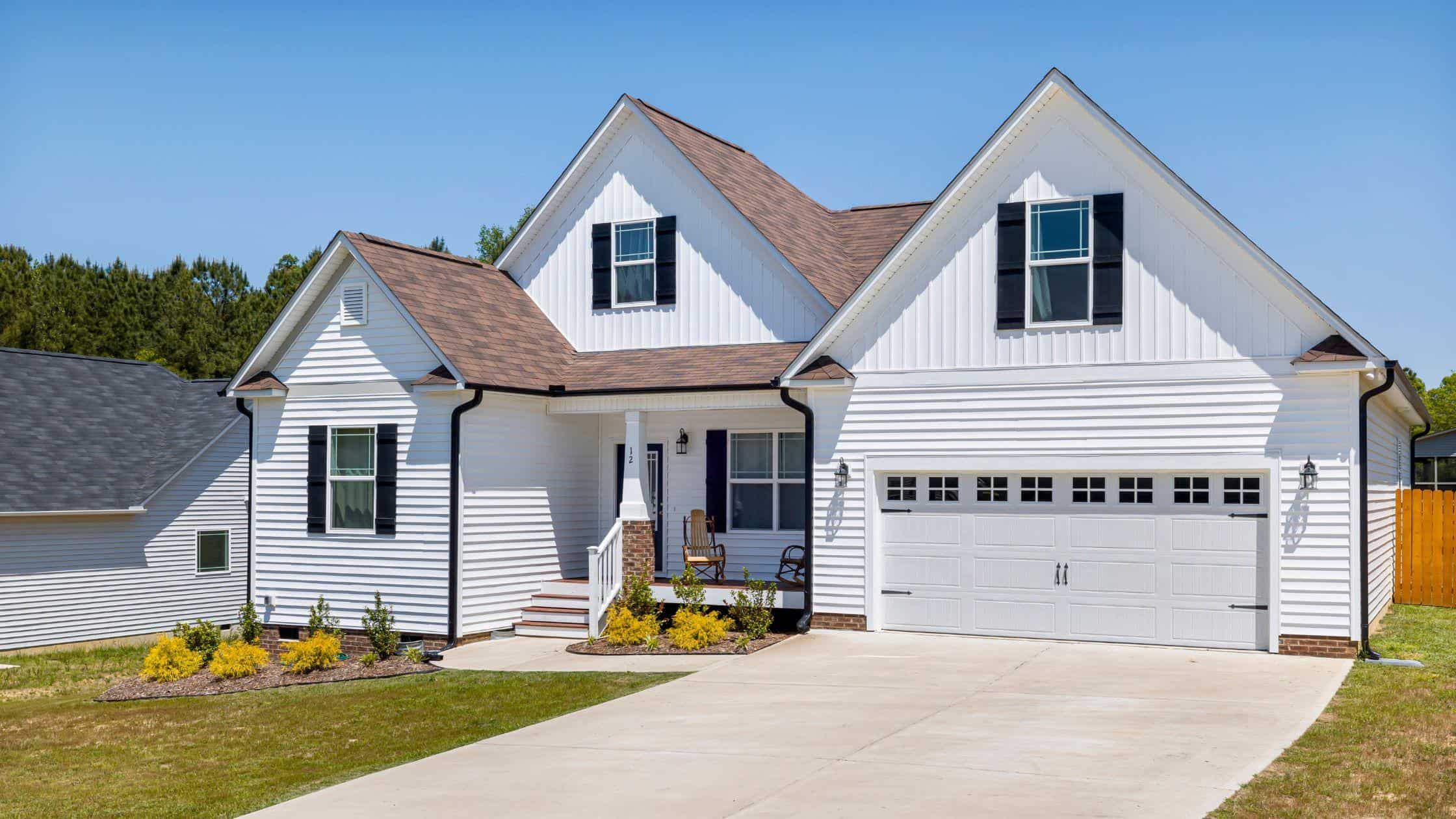 White house with a spacious driveway and well-maintained lawn, showcasing professional home renovati.