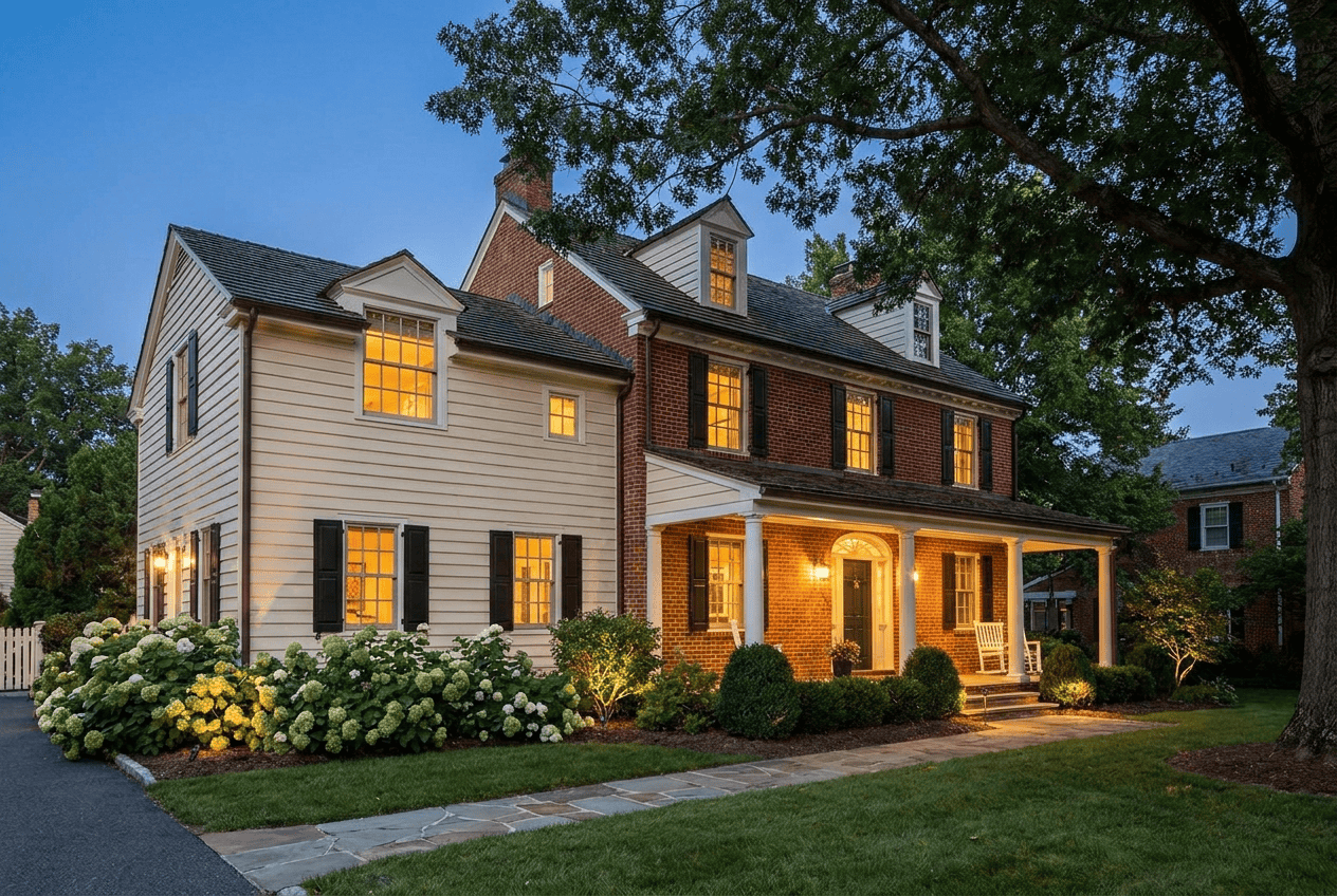 Beautifully lit historic house with lush garden and mature trees at dusk.